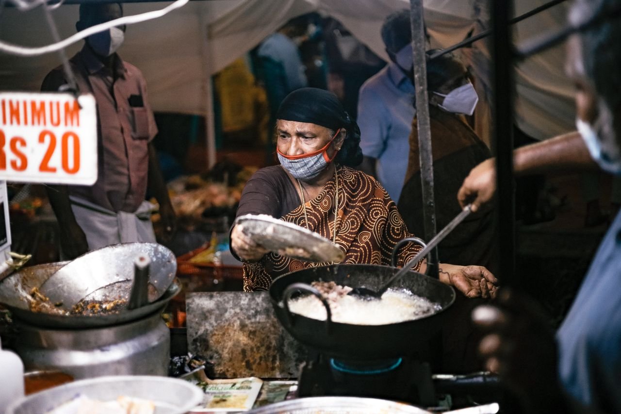 Elderly woman frying food at a bustling night market, showcasing traditional street food preparation.